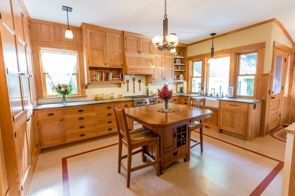 Bright kitchen with wooden cabinets, central island table, and large windows letting in warm light