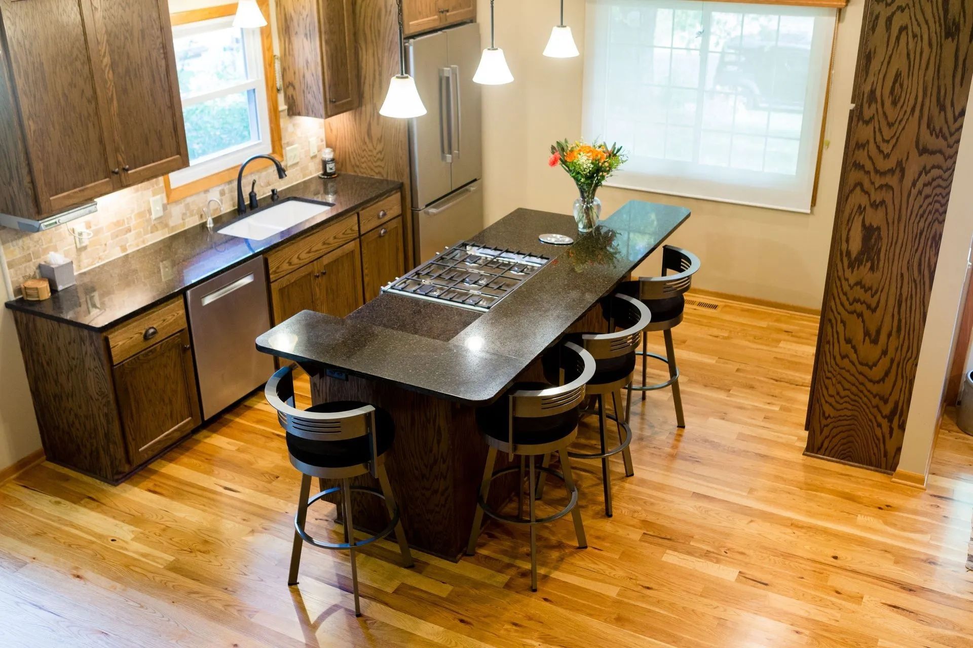 Modern kitchen with island, bar stools, wooden floors, and hanging pendant lights