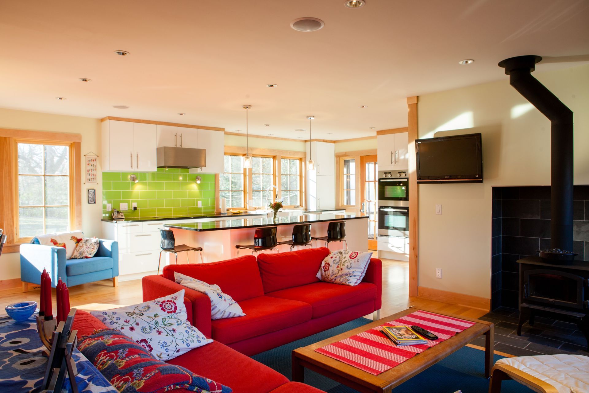 Bright living space with red sofa, kitchen, fireplace, and windows.