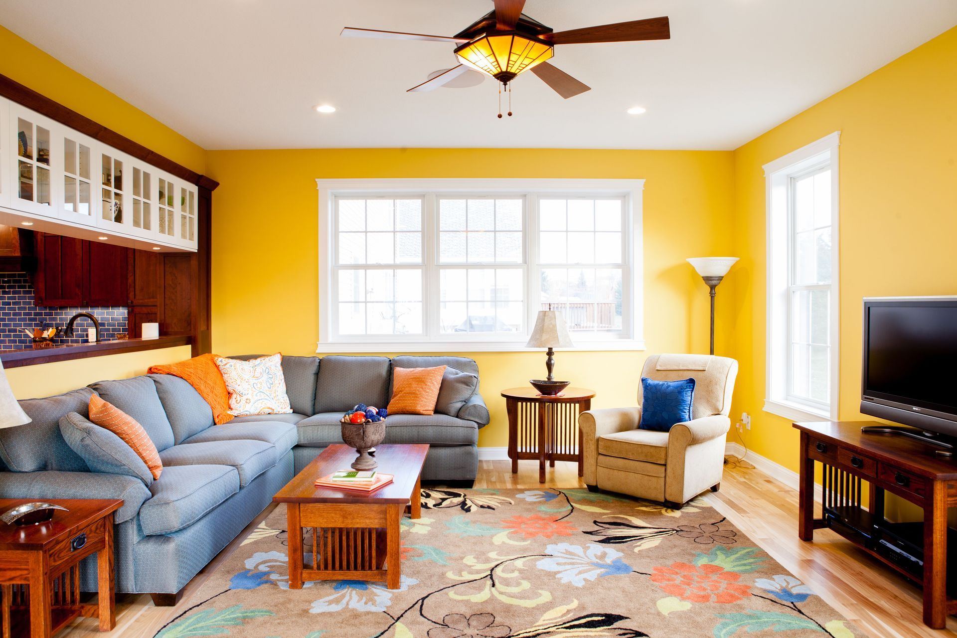 Living room with yellow walls, blue sectional sofa, and floral rug.
