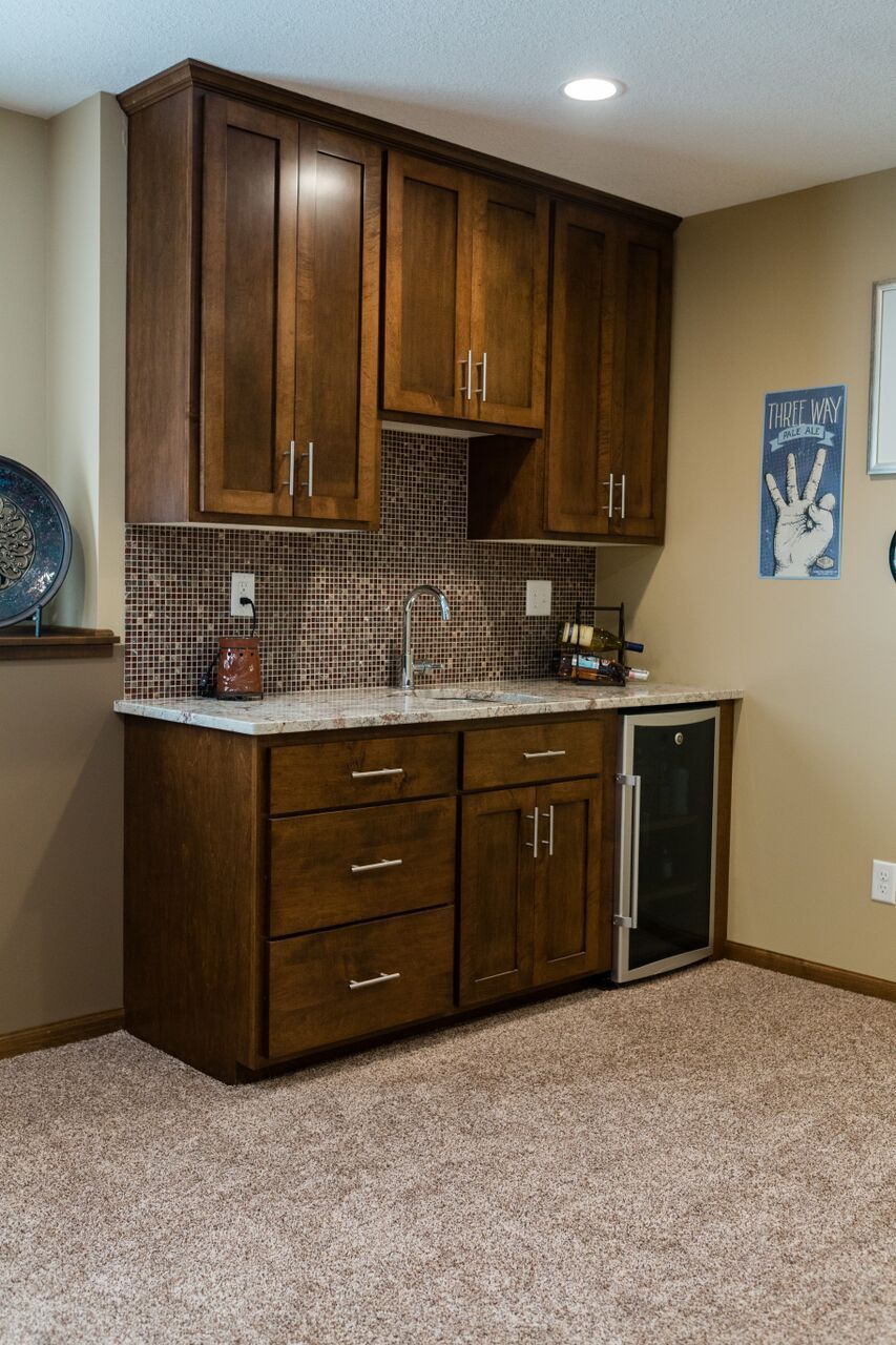 Dark wood bar with upper cabinets, granite countertop, tile backsplash, and a wine cooler.