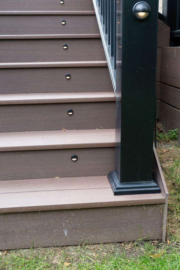 Composite deck stairs with inset lights. Black railing post. Brown steps with green grass.