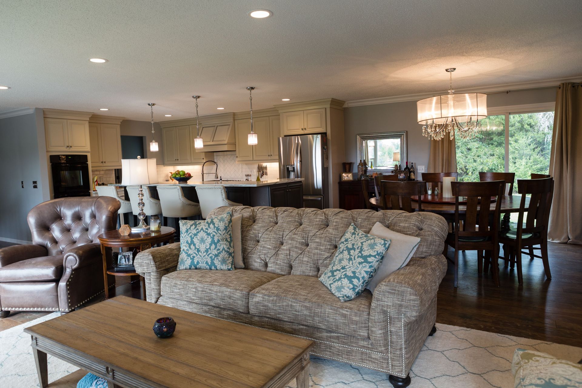 Cozy living space with a tufted sofa, open to a kitchen and dining area with wood floors and neutral tones.