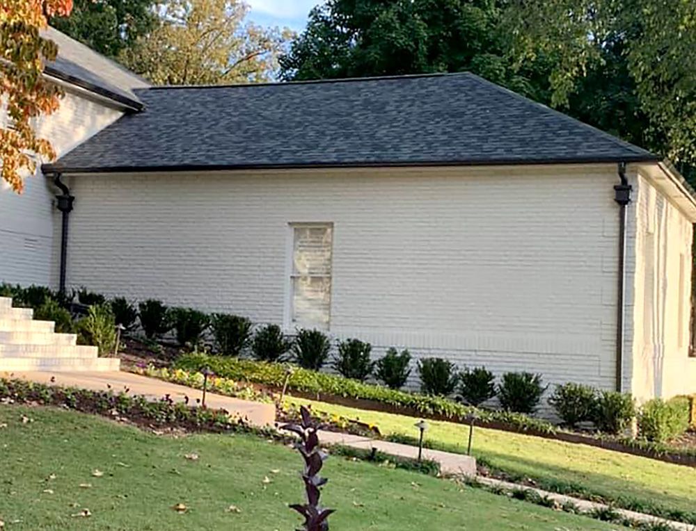A white house with a black roof is sitting on top of a lush green hillside.