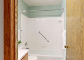 Baño vacío con azulejos blancos, bañera, estante de cristal y barra de apoyo.