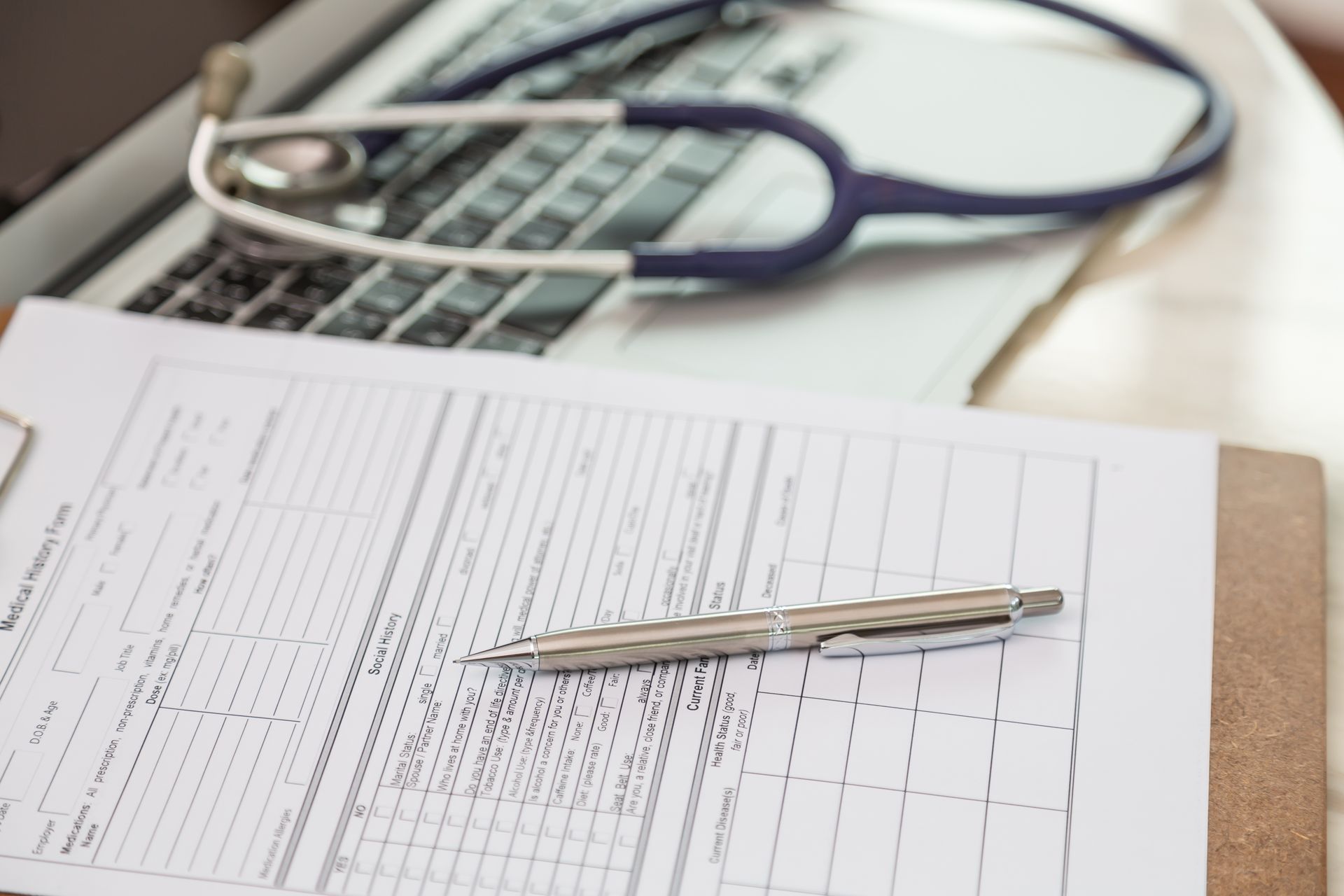 Medical clipboard with pen, laptop, and stethoscope.