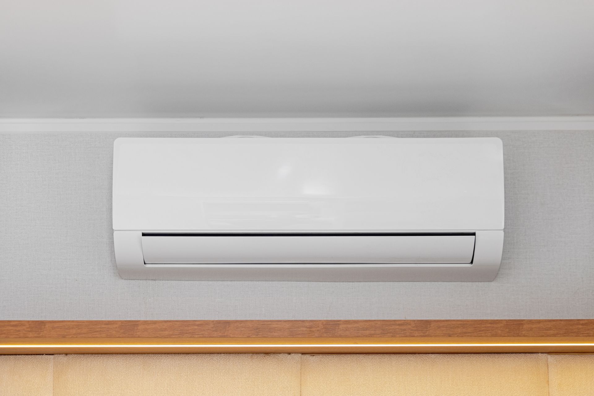 White wall-mounted air conditioner above a wooden trim on a light gray wall