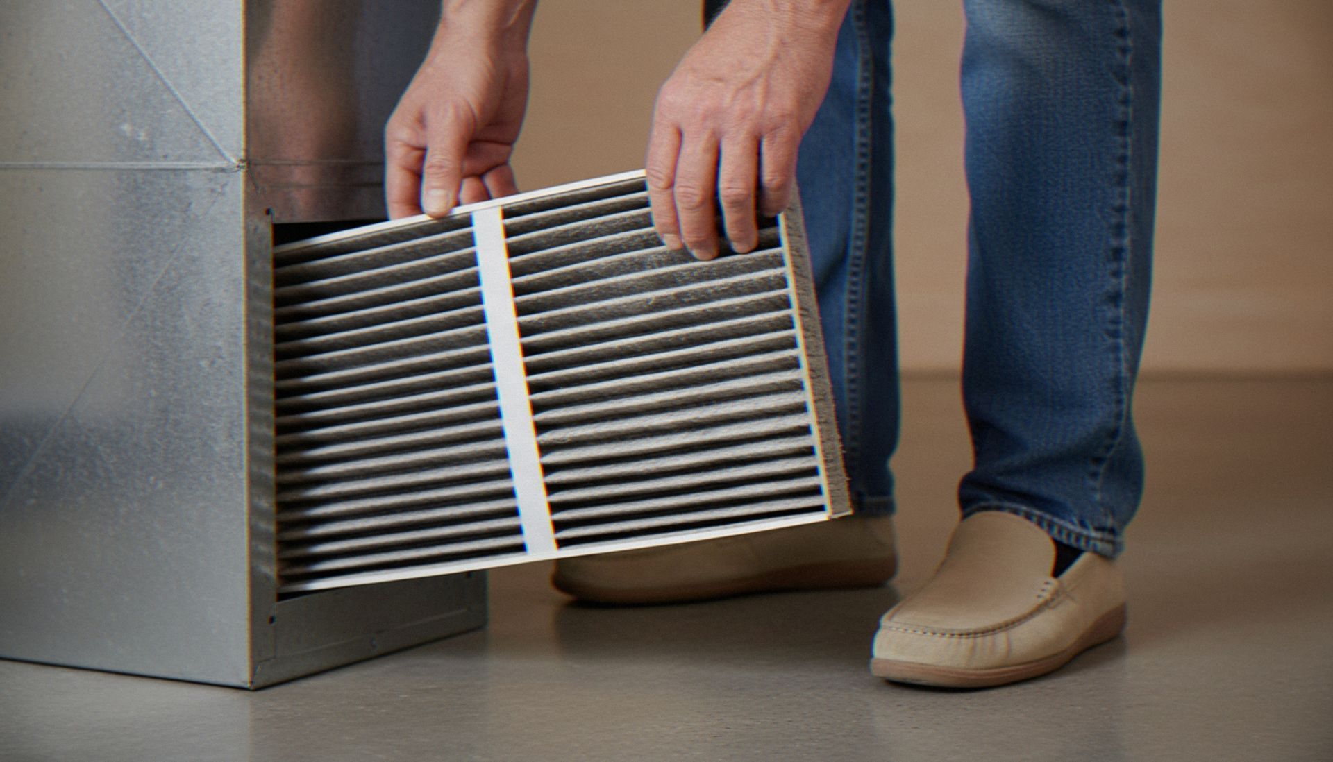 Person holding a pair of white HVAC air filters beside a wall in a room