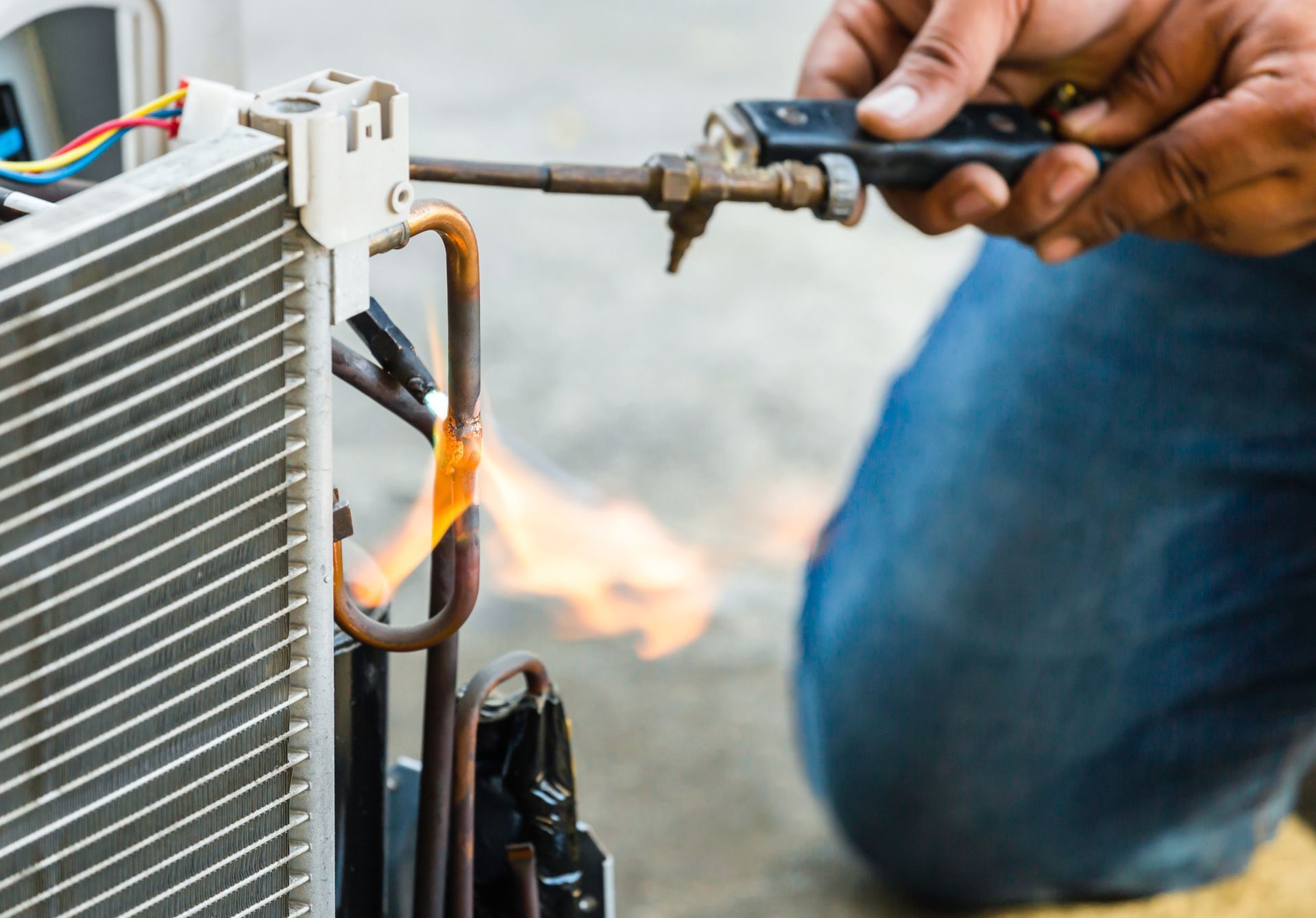 Technician using a torch to repair a flaming HVAC condenser unit outdoors
