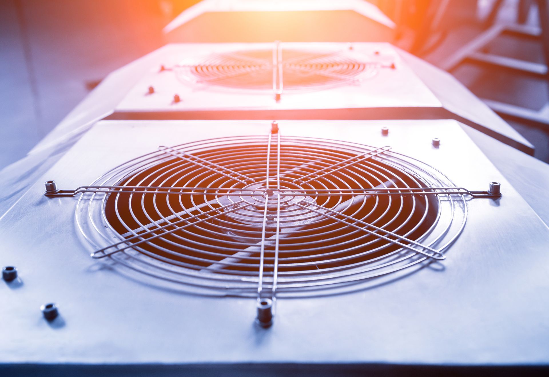 Close-up of a metal cooling fan grille on a white electronic device with orange light