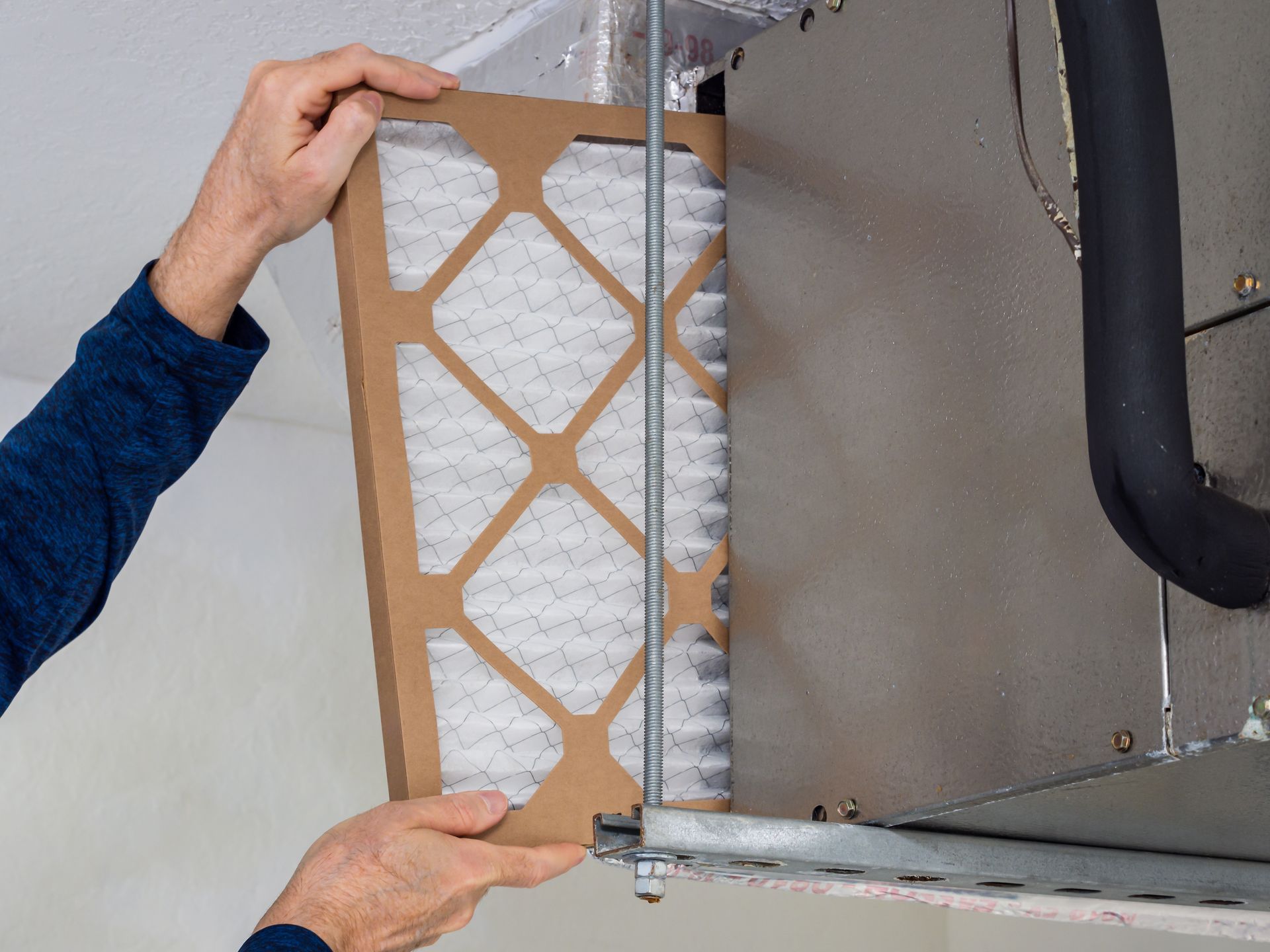 Hands installing a tan air filter inside an HVAC unit
