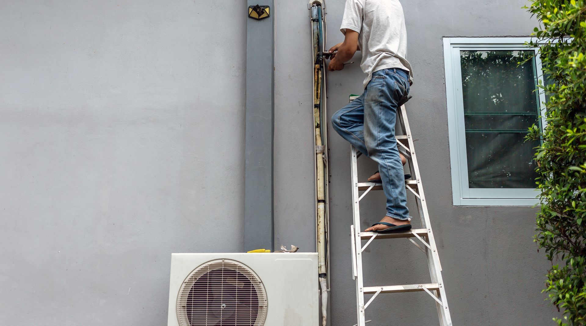 Worker on a ladder repairing an exterior wall beside a window and air conditioner unit