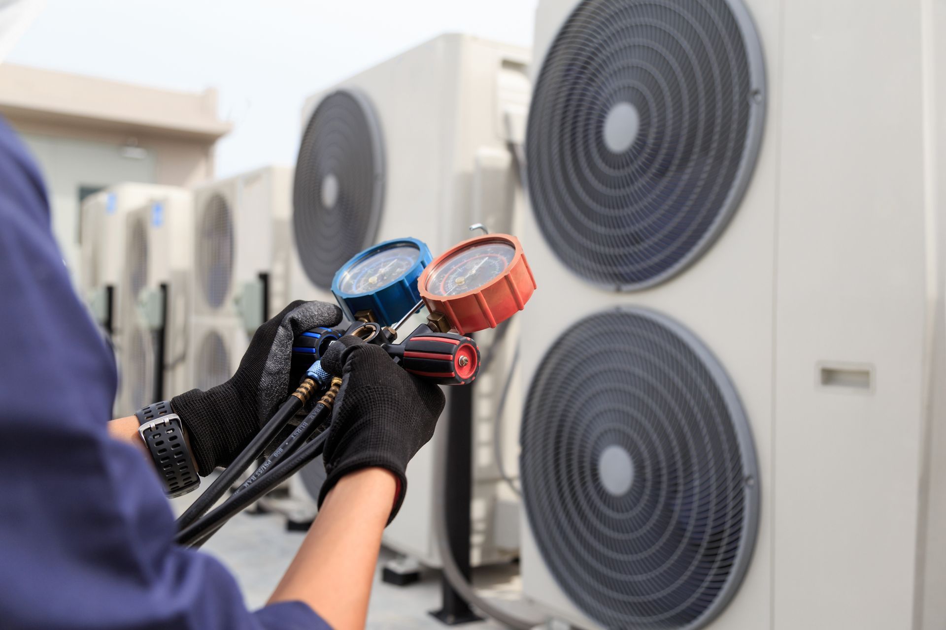Technician holding refrigerant gauges near outdoor air conditioner units