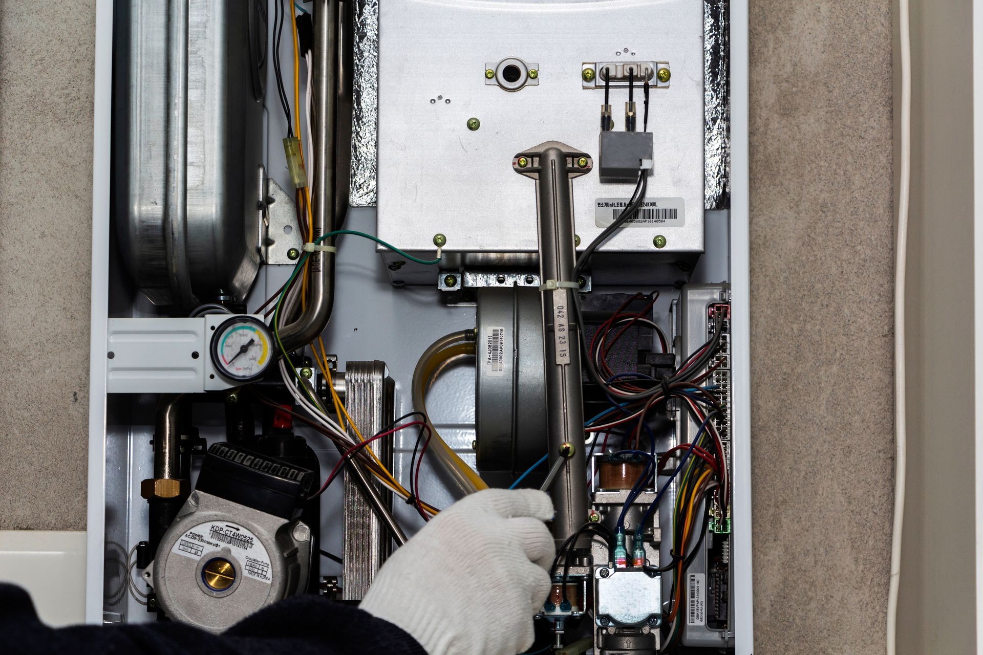 Technician in white gloves inspecting wiring and components inside an open HVAC unit.