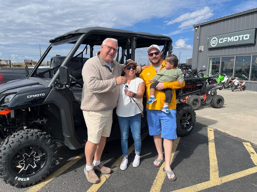 A group of four people standing in front of a dealership posing with a newly purchased black off-road vehicle.