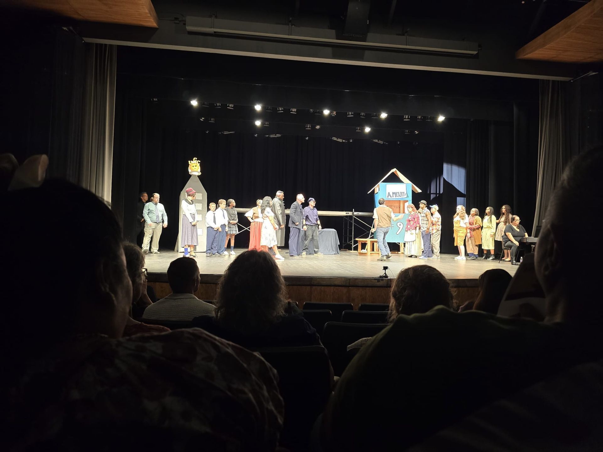 Theater stage with a group of performers in costume under bright lights, viewed from the audience.
