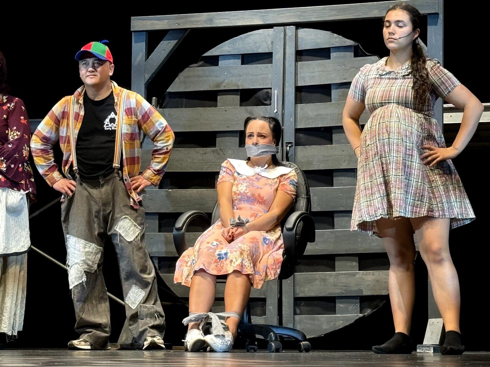 Three people posing on a stage set, with one seated in the center and two standing beside her