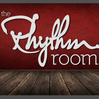 “The Rhythm Room” sign in white script on a red wall above a wooden floor