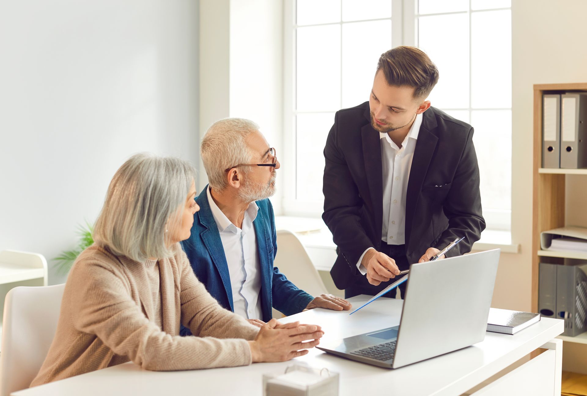 Three coworkers discussing documents around a laptop in a bright office
