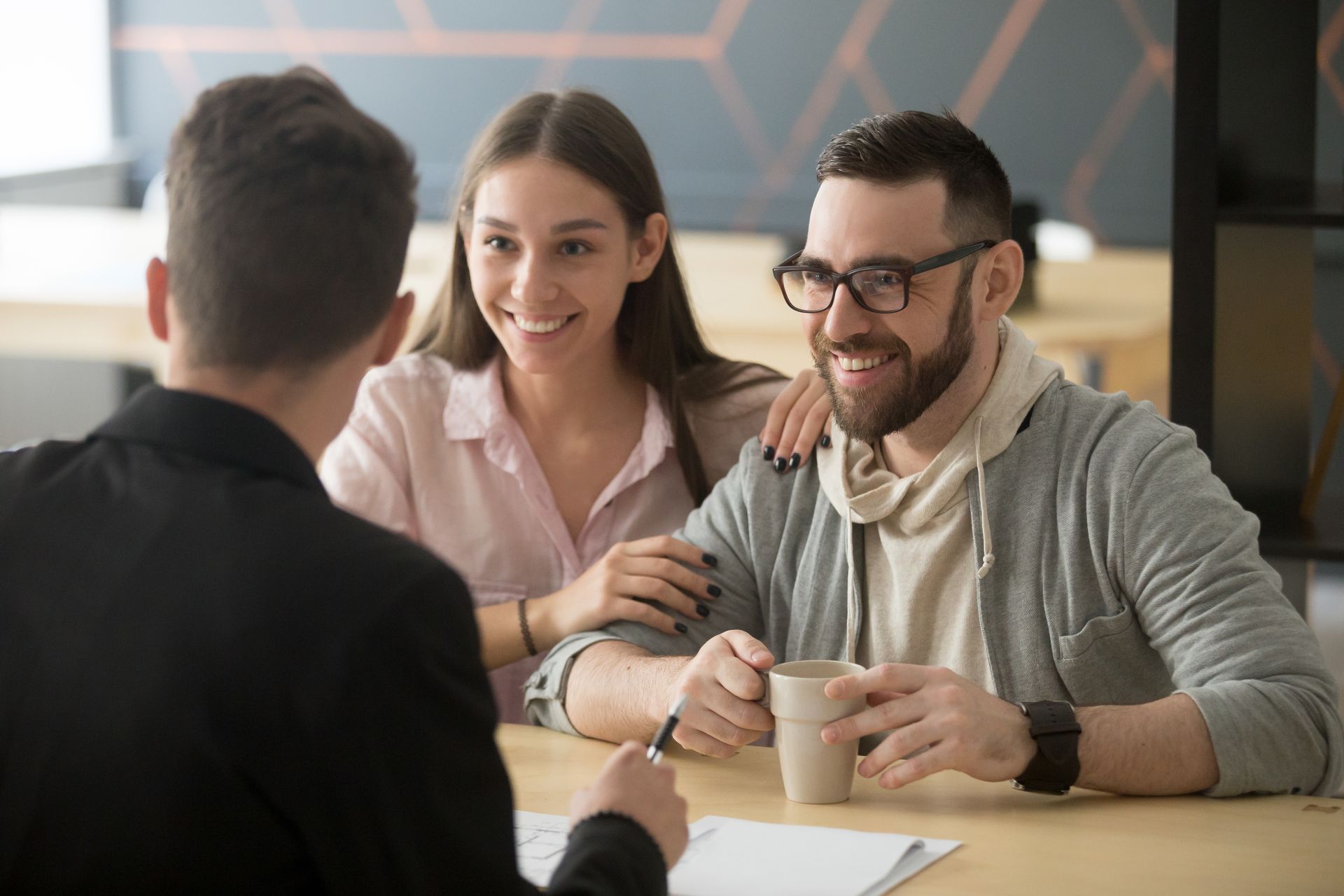 Three people chatting at a café table, smiling with coffee cups and papers.