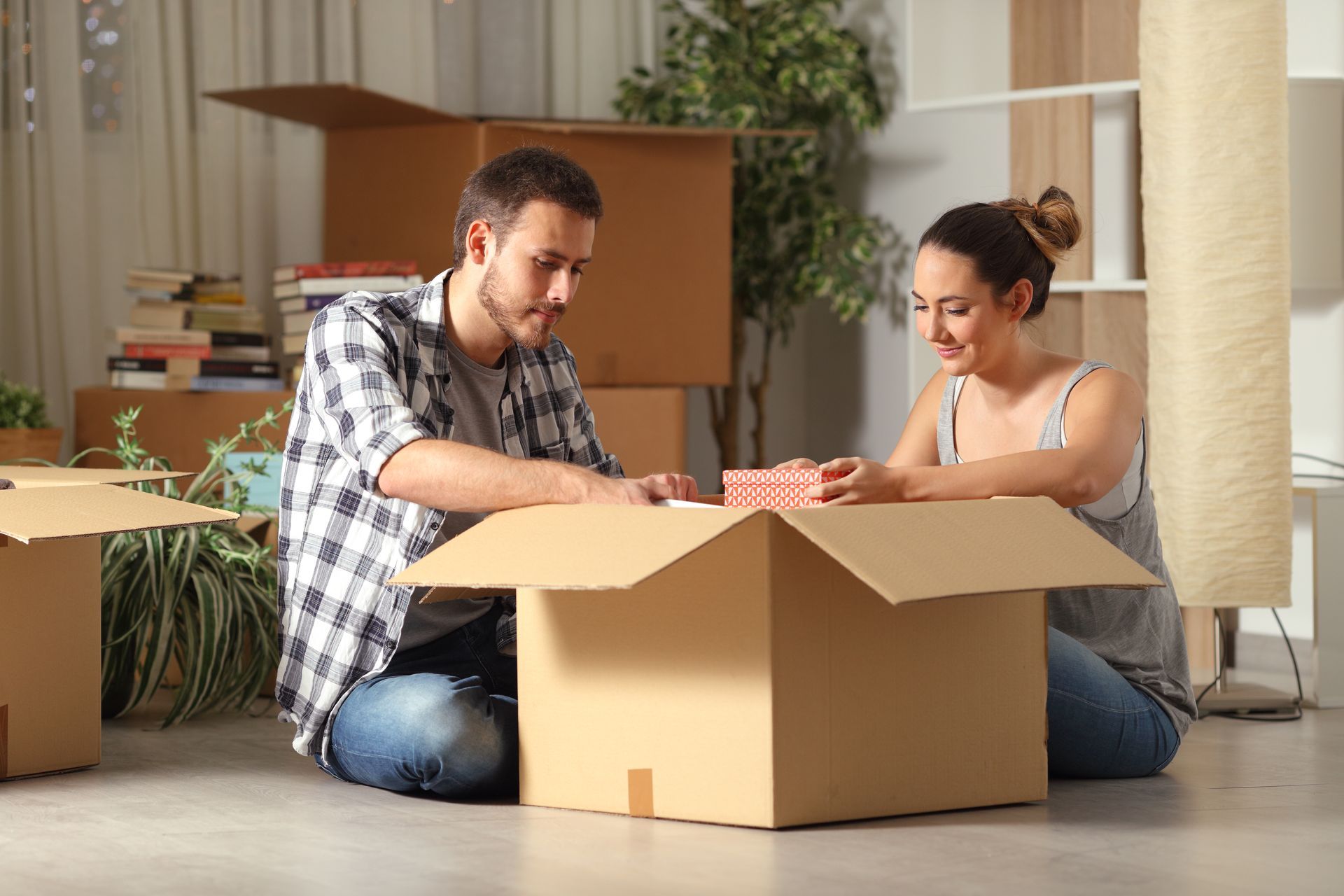 Two people unpacking a cardboard box in a bright living room