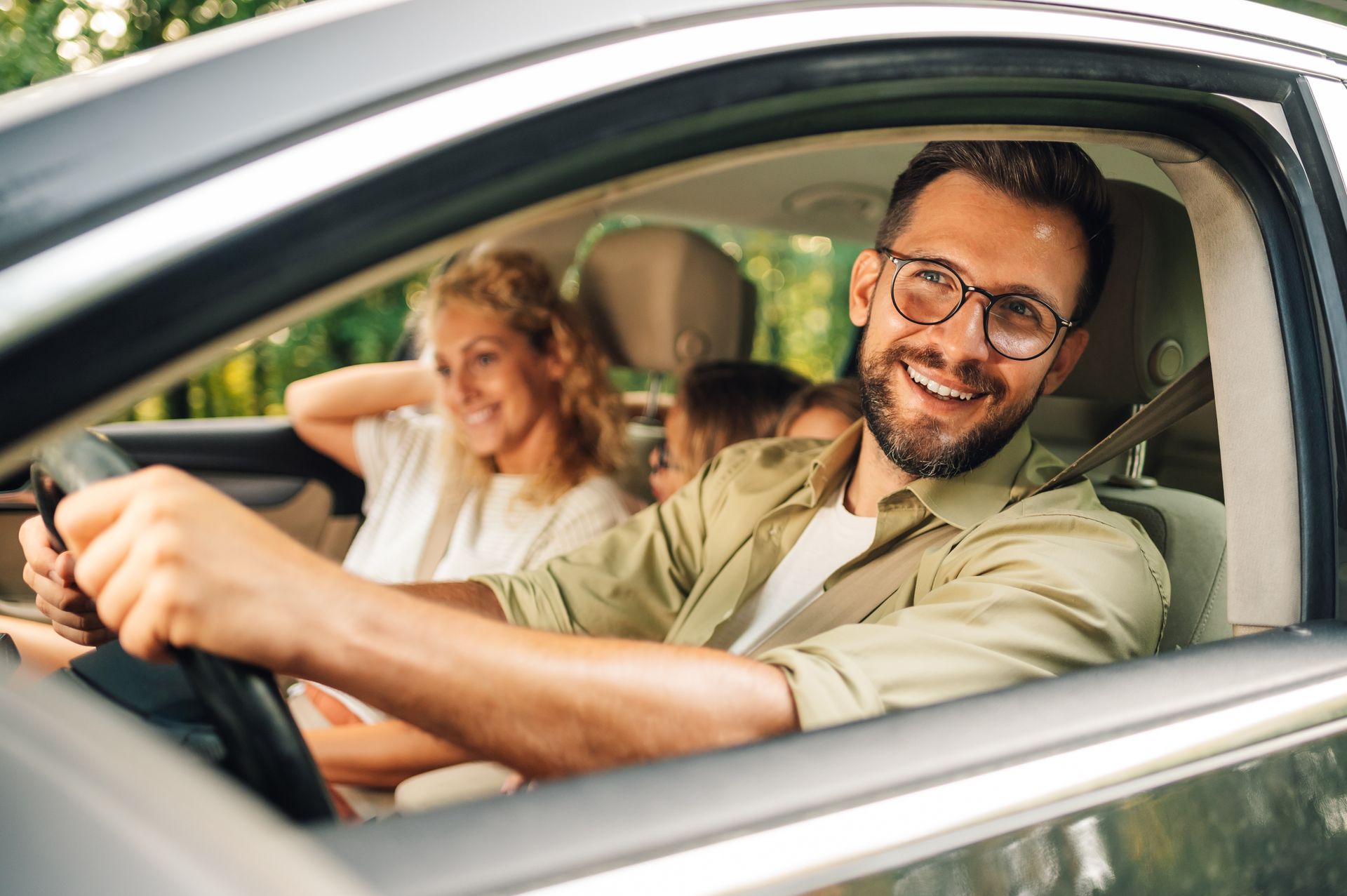 Smiling driver in a car with a passenger in the back seat, seen through the open window