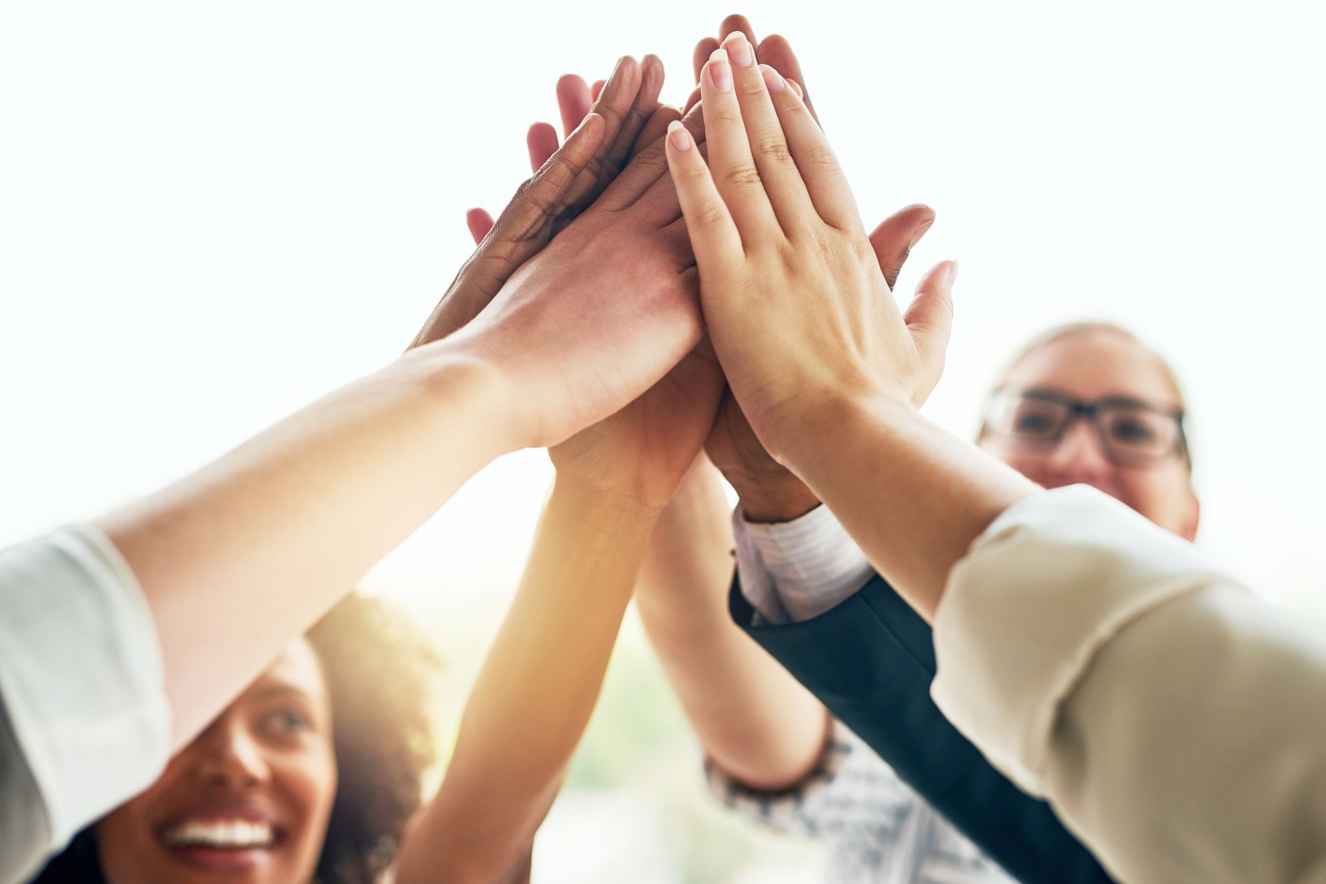 Hands of a diverse team meeting in a high-five, with smiling faces in the background
