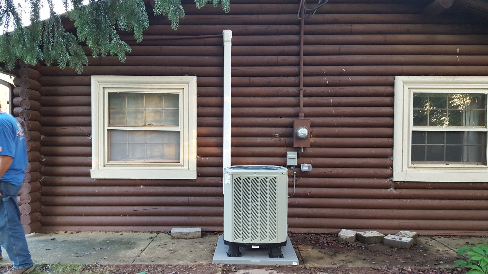 Brown log cabin exterior with a white window, utility vent, and outdoor HVAC unit along the wall