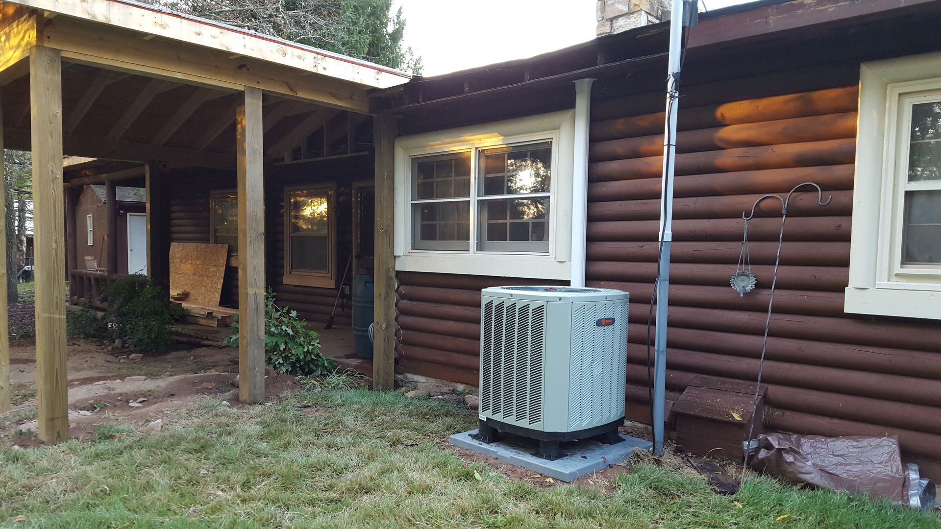 Log cabin exterior with window, covered porch, and outdoor AC unit on a grassy yard