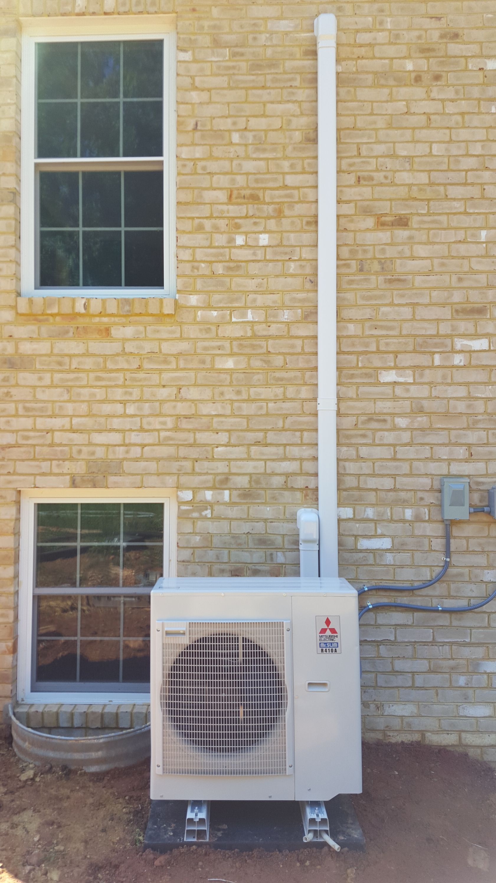 Outdoor air-conditioning unit mounted against a yellow brick building beneath two windows