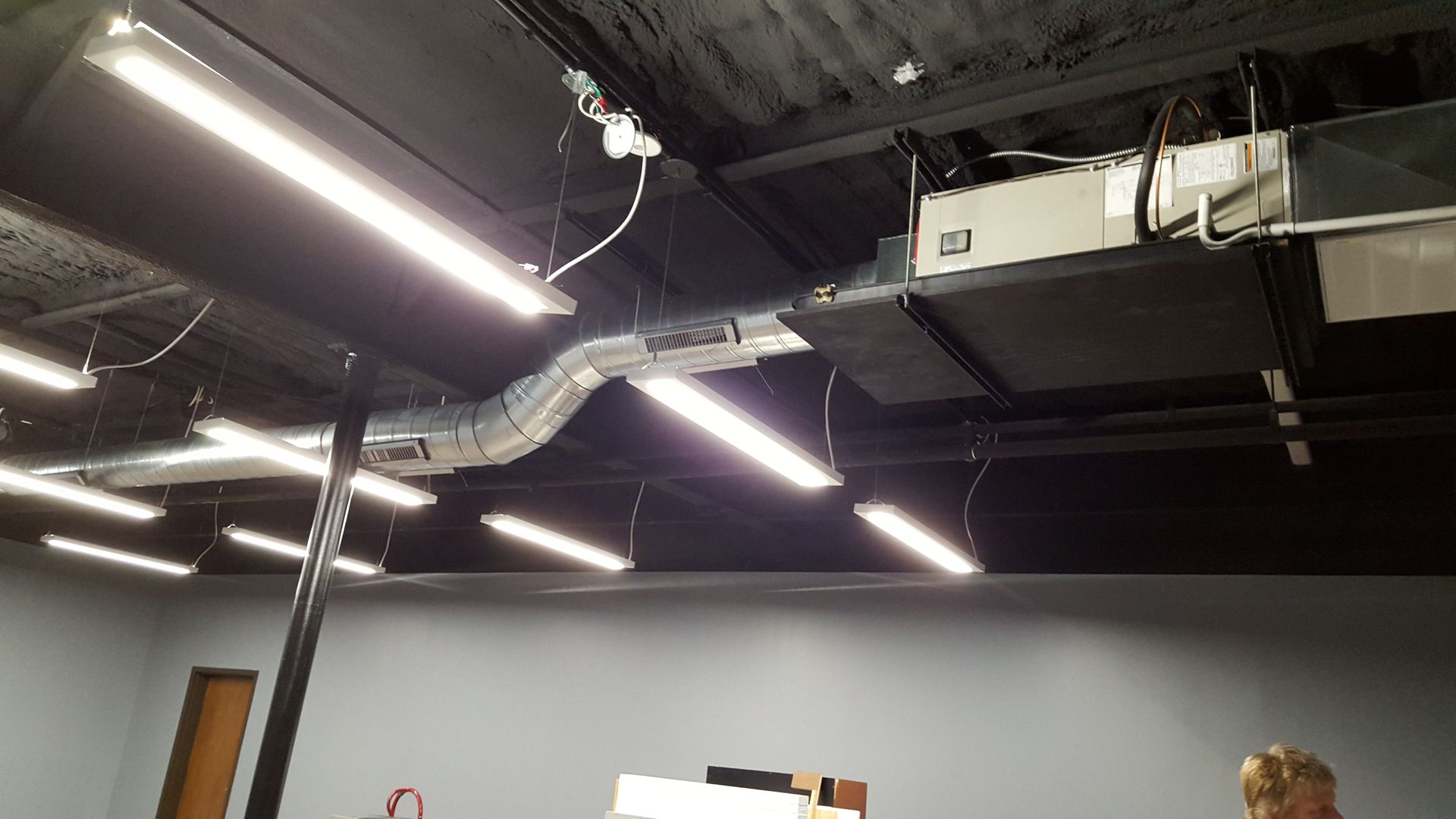 Industrial ceiling with exposed ducts and bright fluorescent lights in a warehouse-like interior