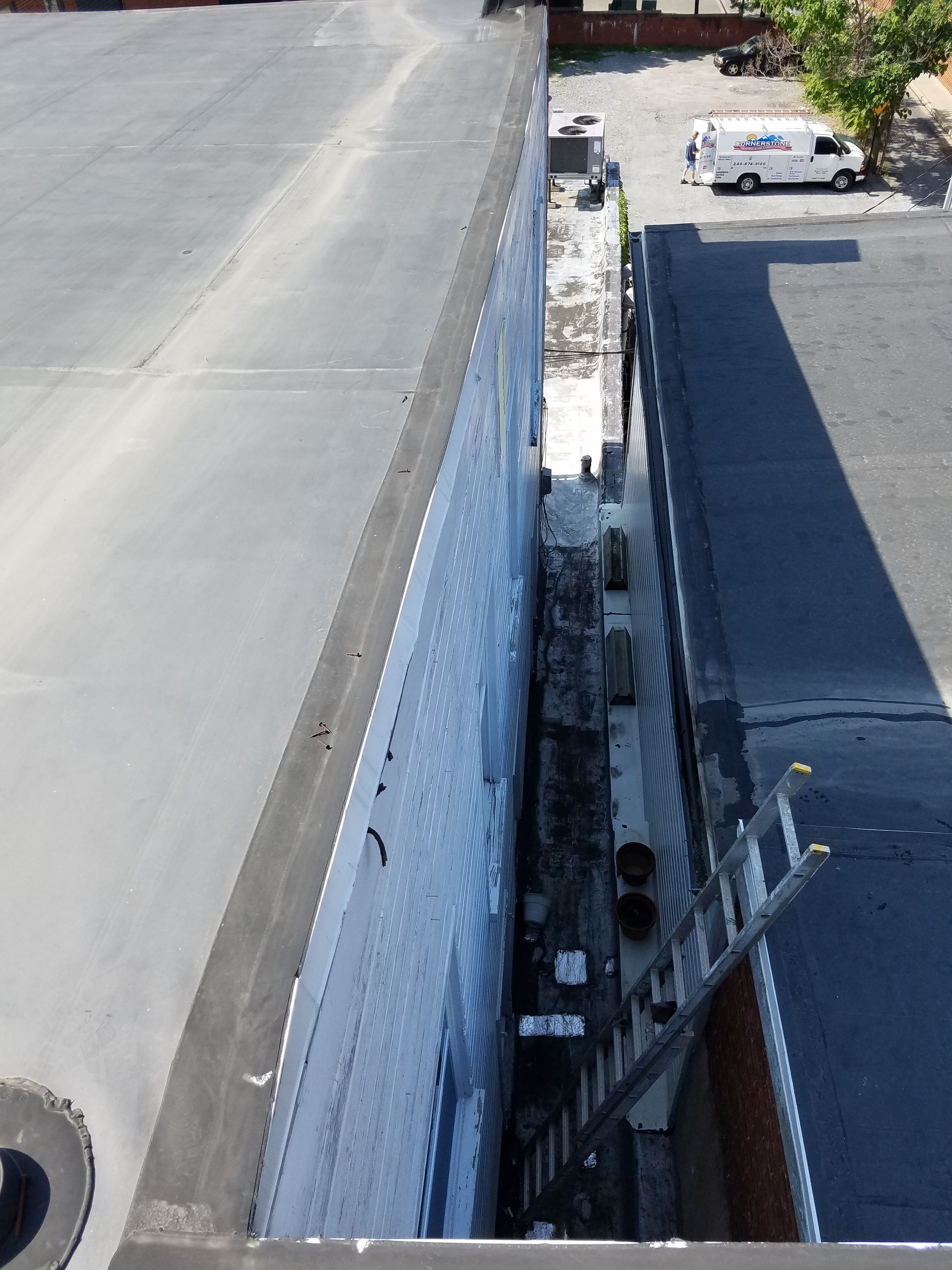 Aerial view of a rooftop edge beside a narrow alley and adjacent parking lot with a white van.