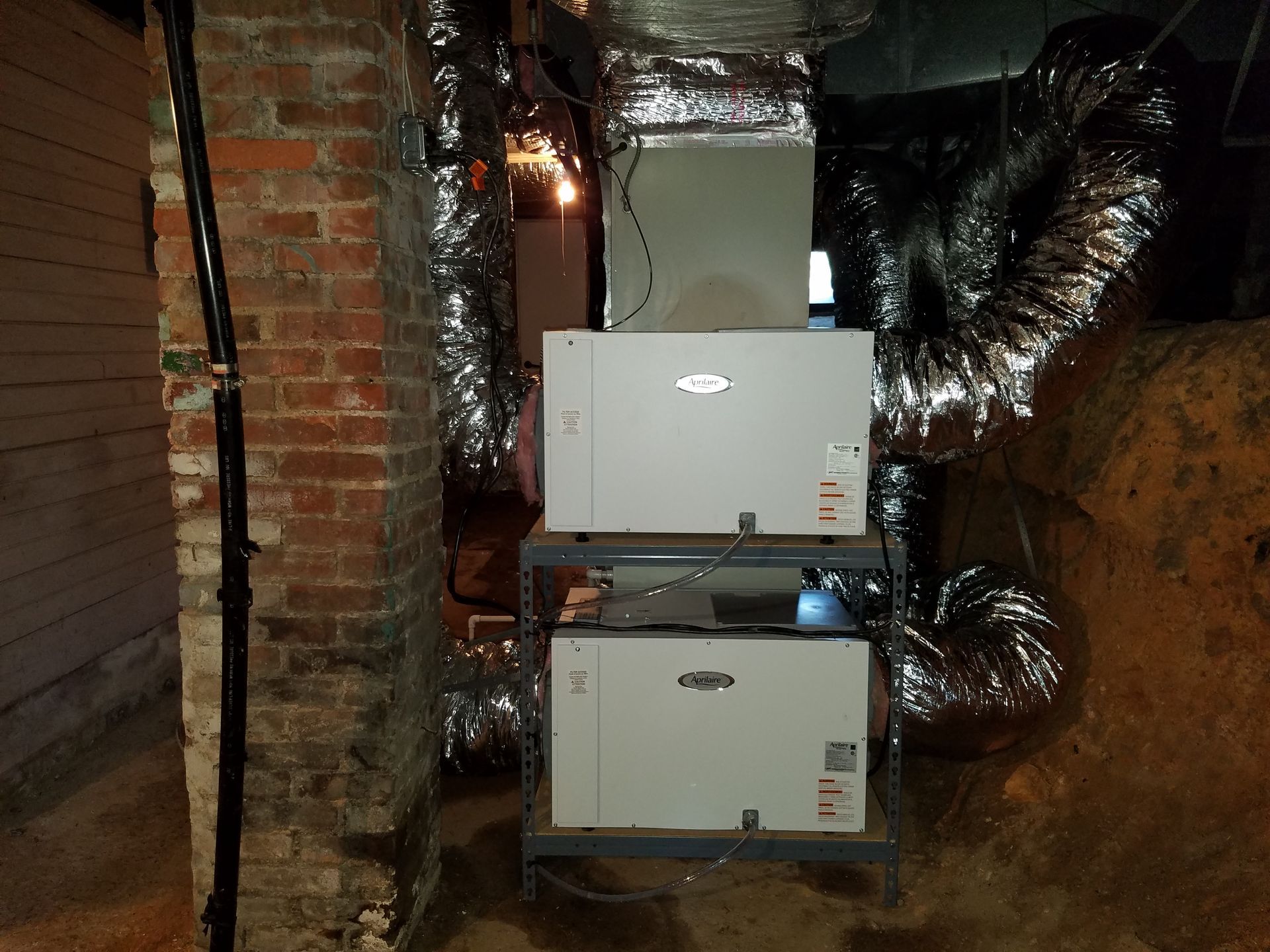 Two white wall-mounted HVAC units in a narrow basement with exposed brick and shiny ductwork.