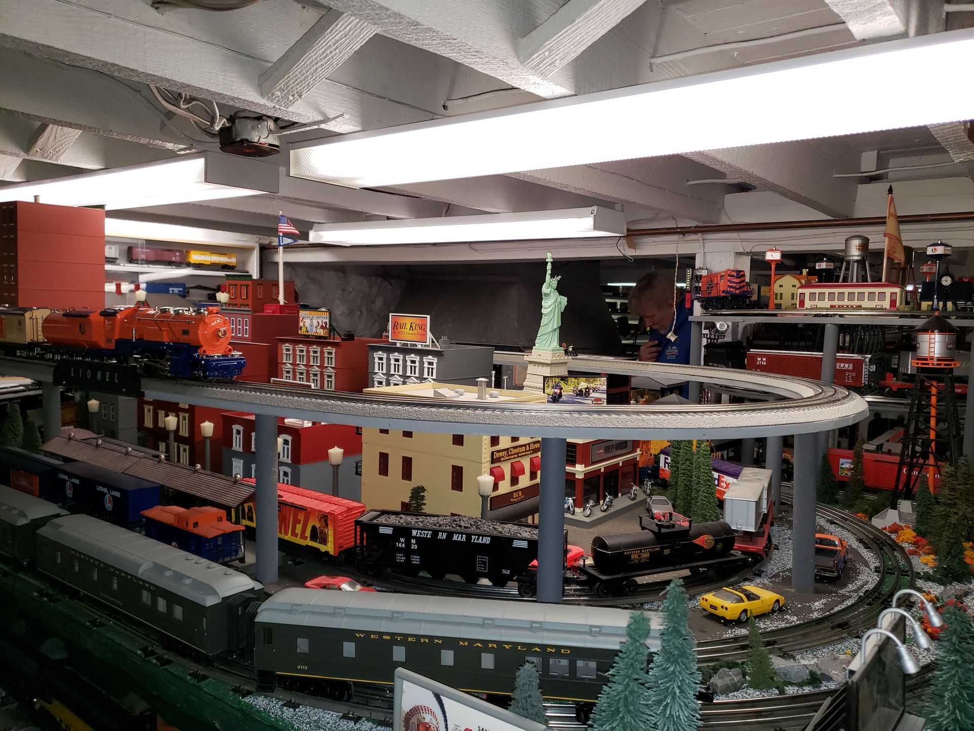 Indoor Lego train layout with looping tracks, buildings, and a red train in a basement room
