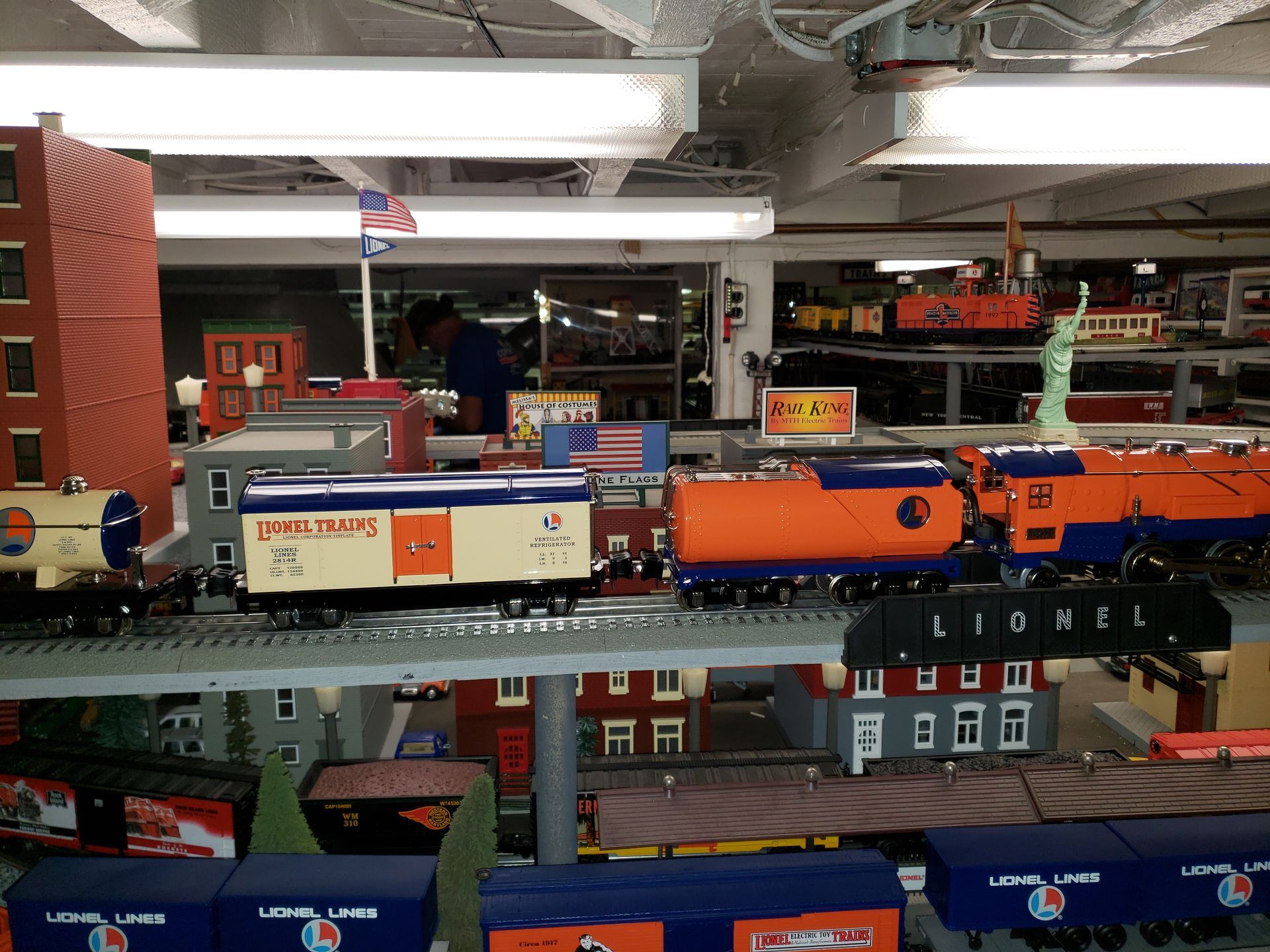 Model train layout with orange and blue locomotives on tracks in an indoor display room