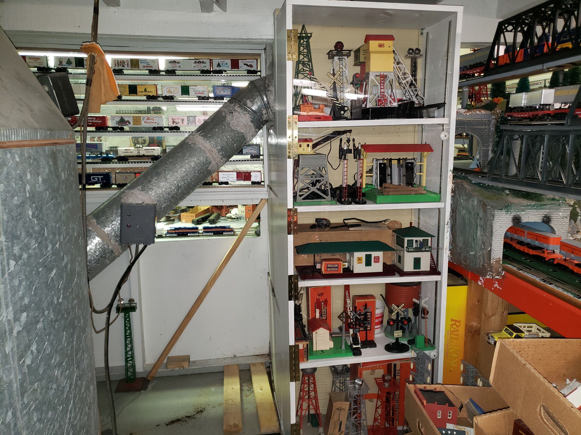 Model train room with shelves of miniature buildings, tracks, and a gray tube in the foreground