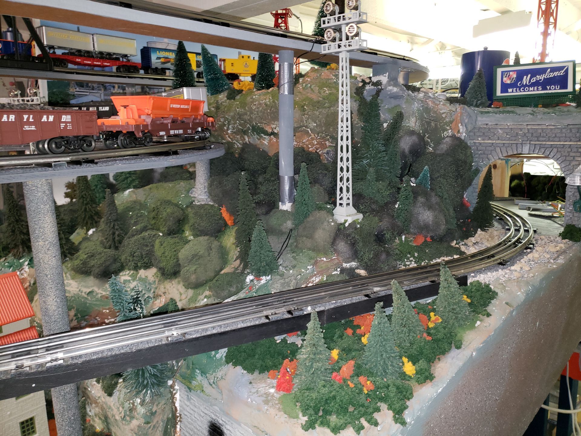 Model train layout with tracks, orange train cars, bridges, trees, and a curved tunnel scene