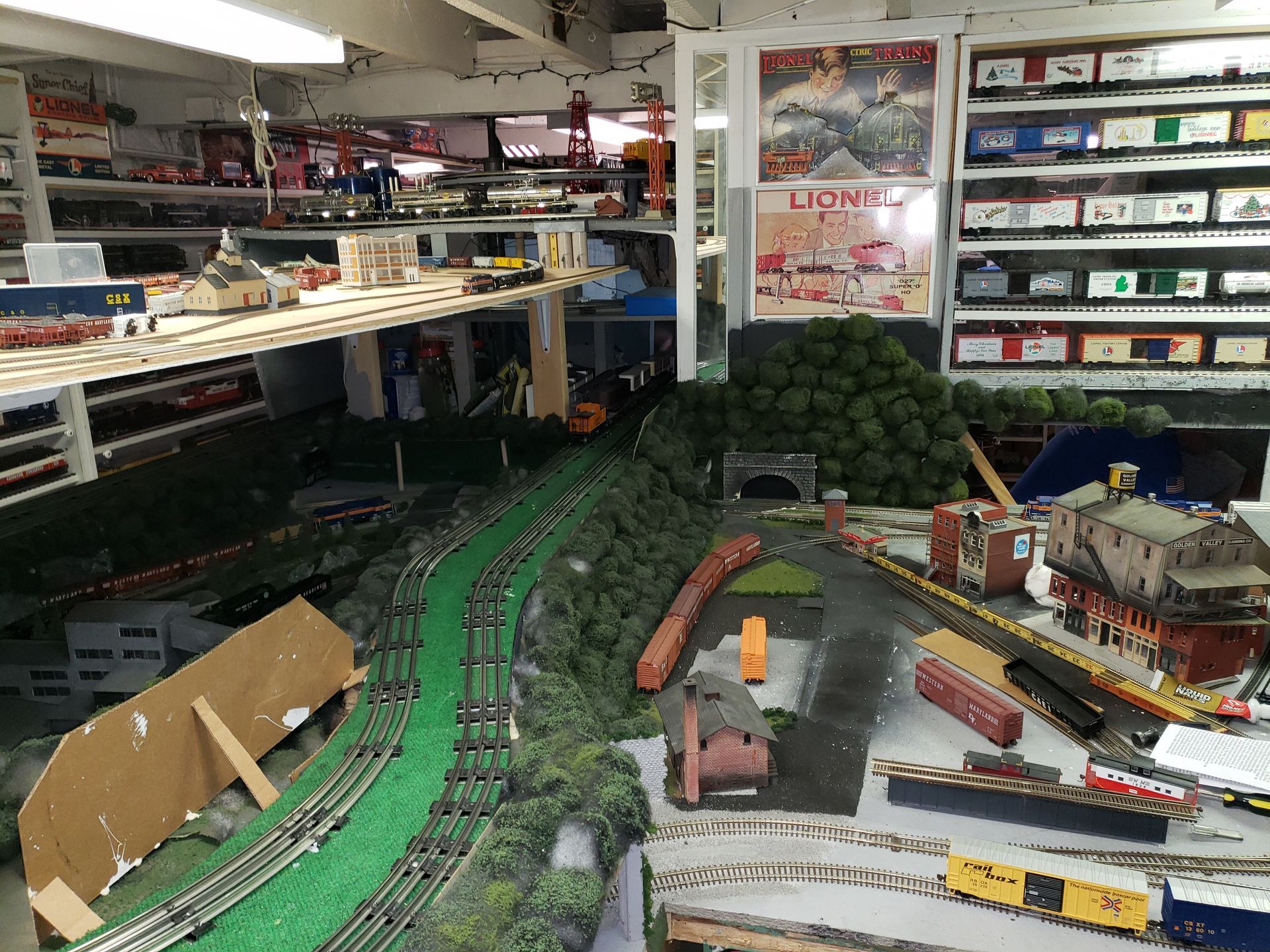 Toy train display with green tracks, model buildings, and trains in a store interior