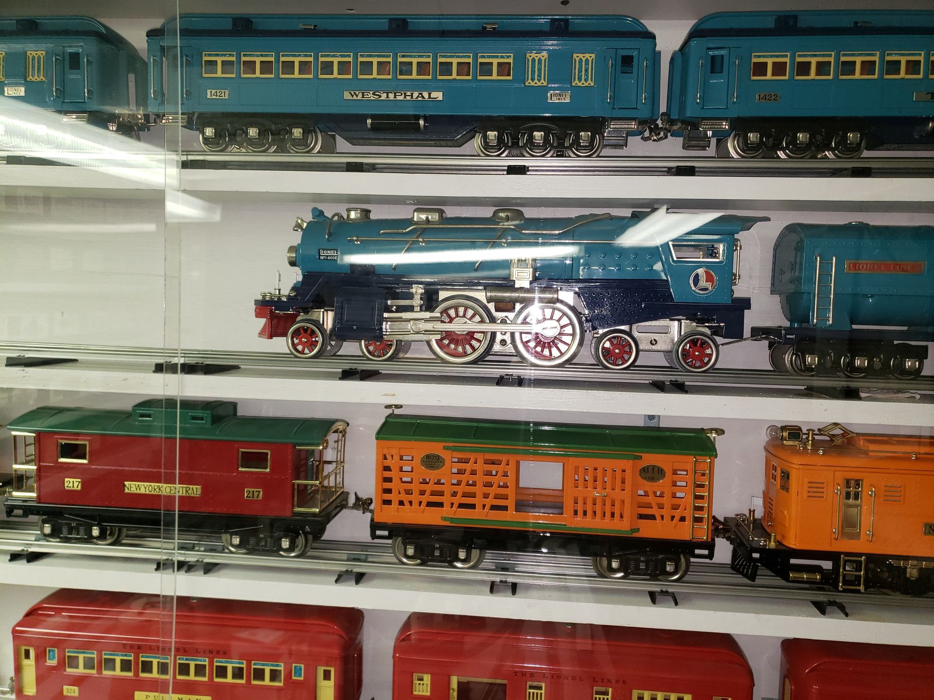 Shelves of colorful model trains, including a blue steam engine and red and orange passenger cars.