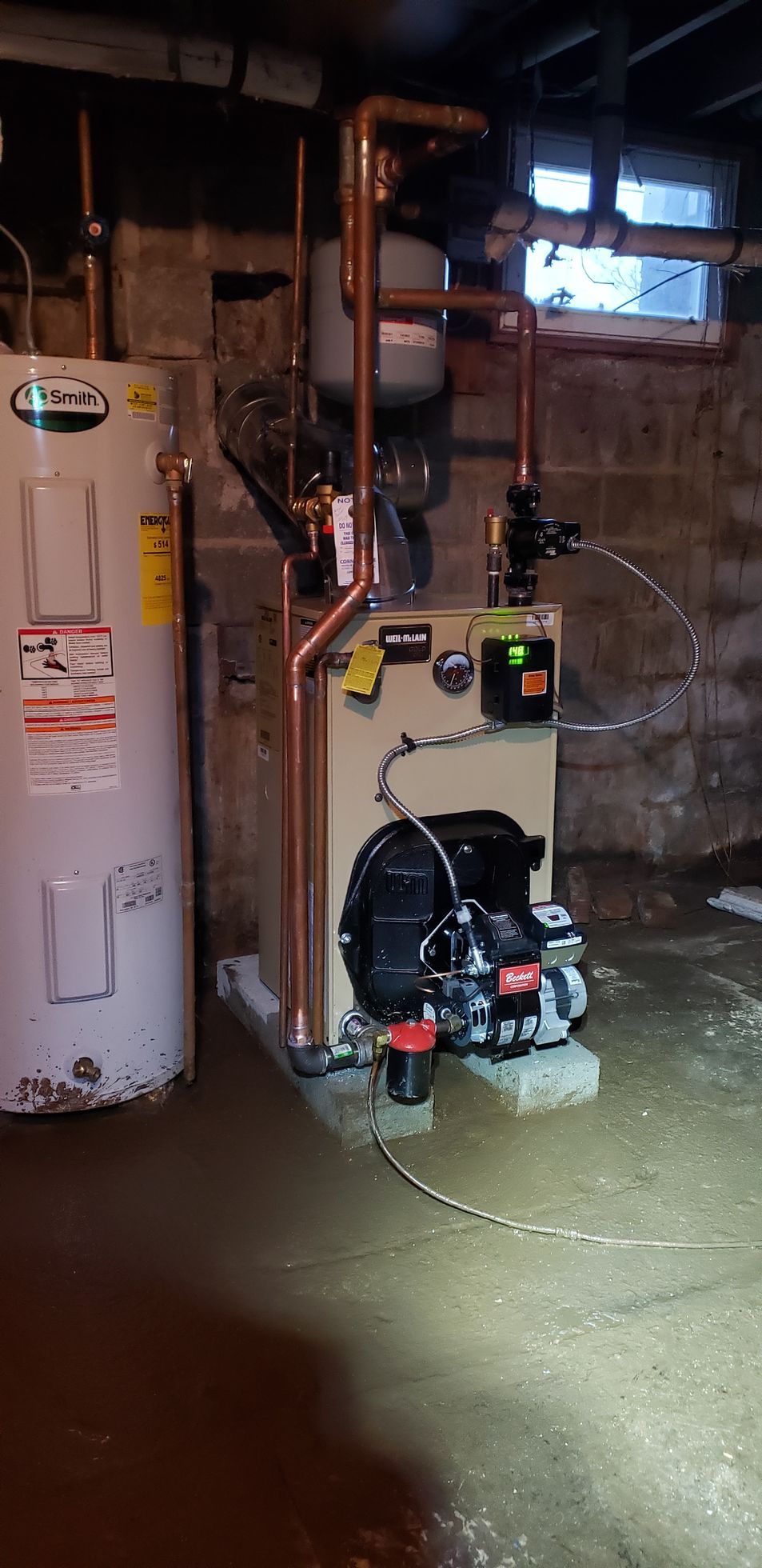 Basement utility area with a white water heater, pumps, pipes, and a control panel on a concrete floor.