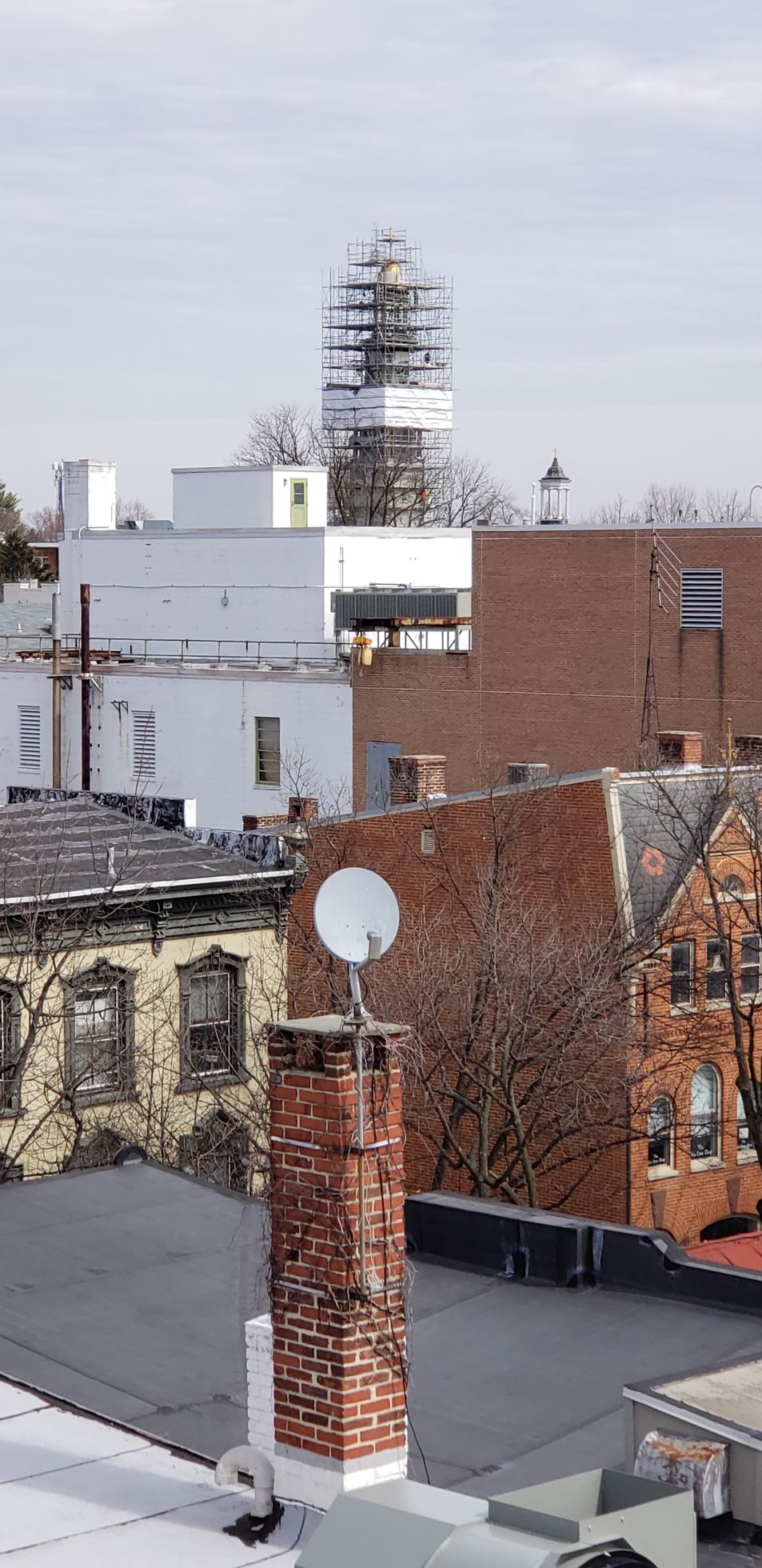 Rooftop cityscape with brick buildings, white rooftops, and a satellite dish in the foreground.