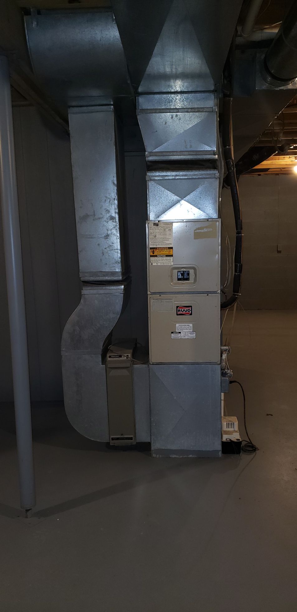Industrial HVAC ductwork and a silver ventilation unit in a basement mechanical room