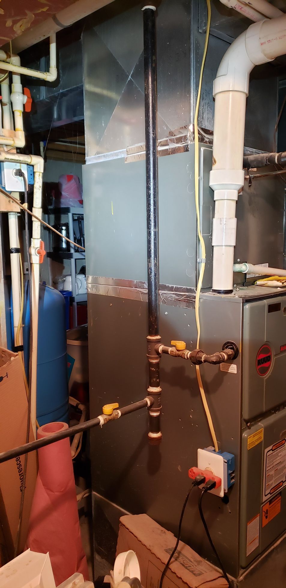 Industrial boiler room with large gray HVAC units, pipes, and valves in a basement setting