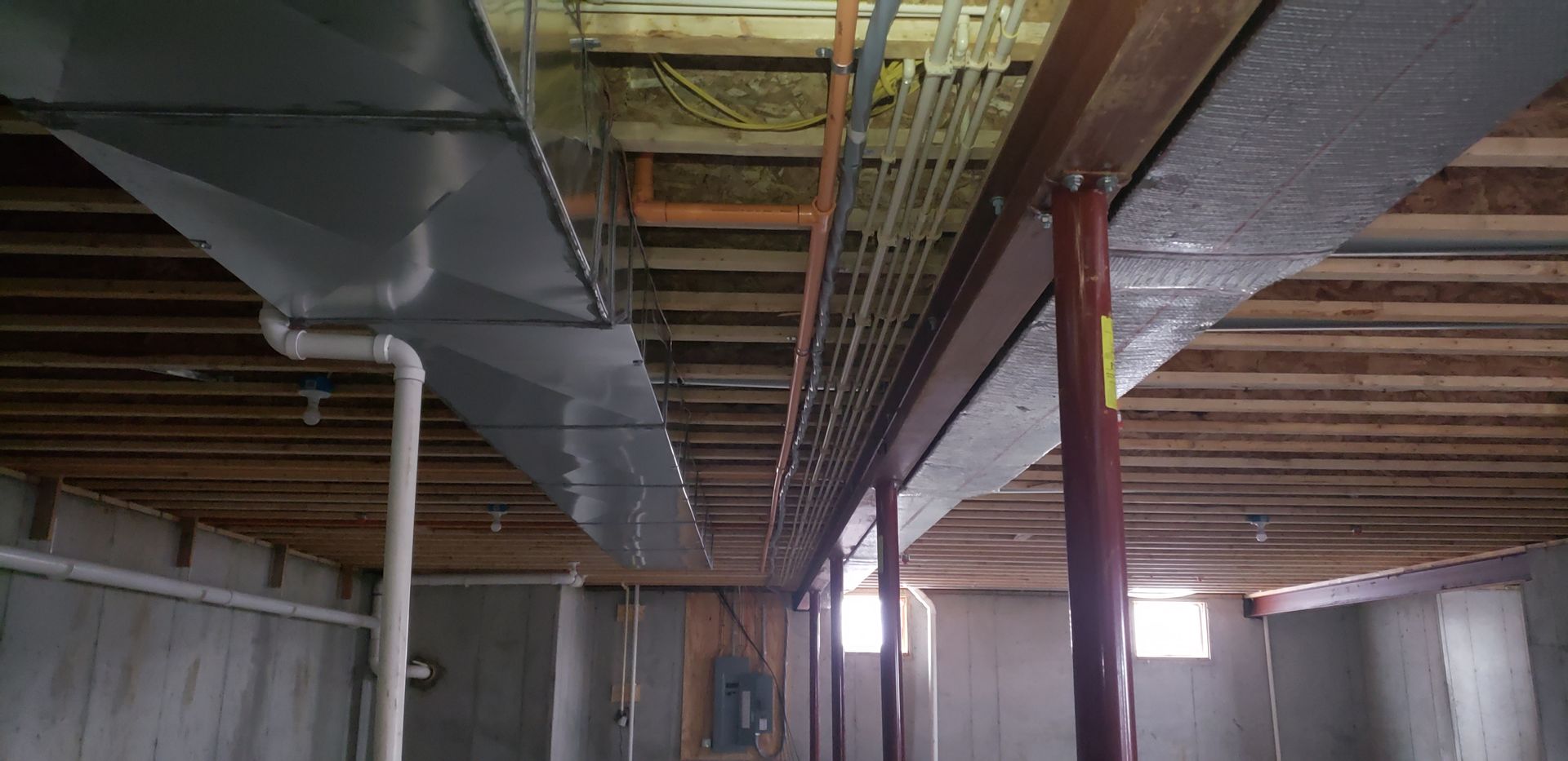 Basement ceiling with exposed ducts, pipes, and wooden beams in an unfinished room