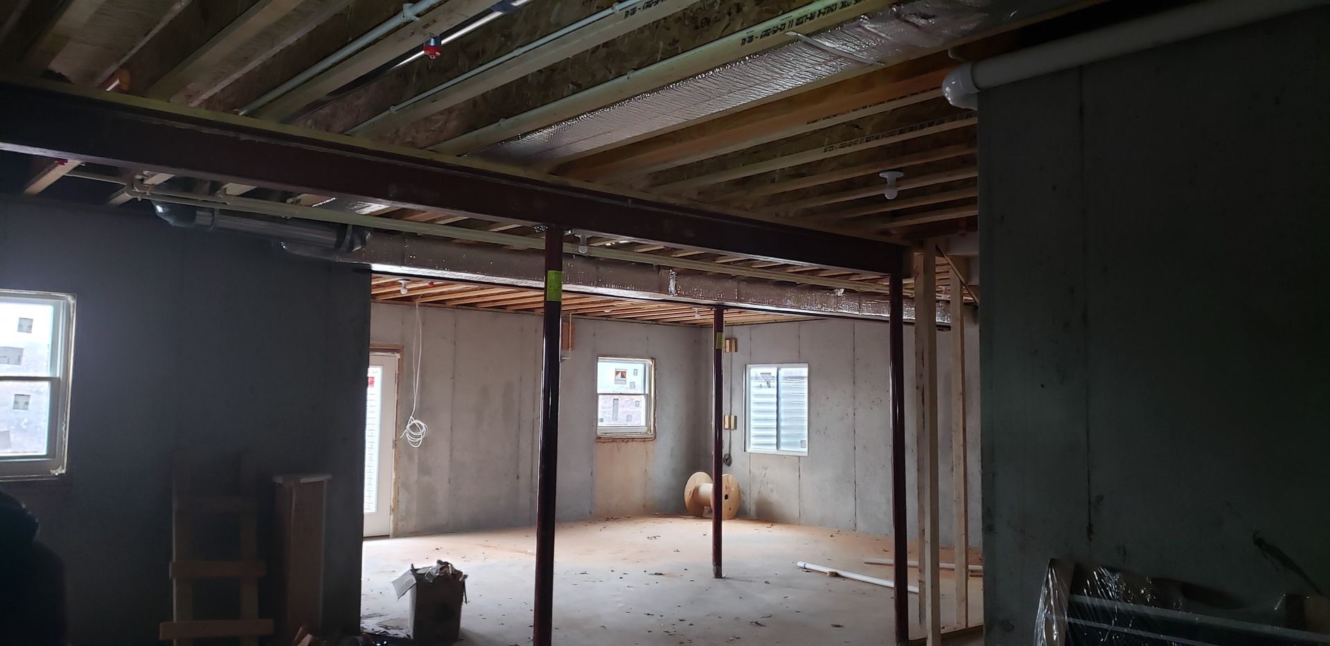 Empty unfinished room with exposed beams, concrete floor, and large open doorway to a brighter space.