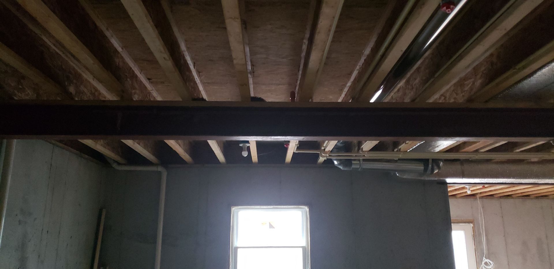 Interior of an unfinished room with exposed wooden ceiling beams and a small window letting in daylight