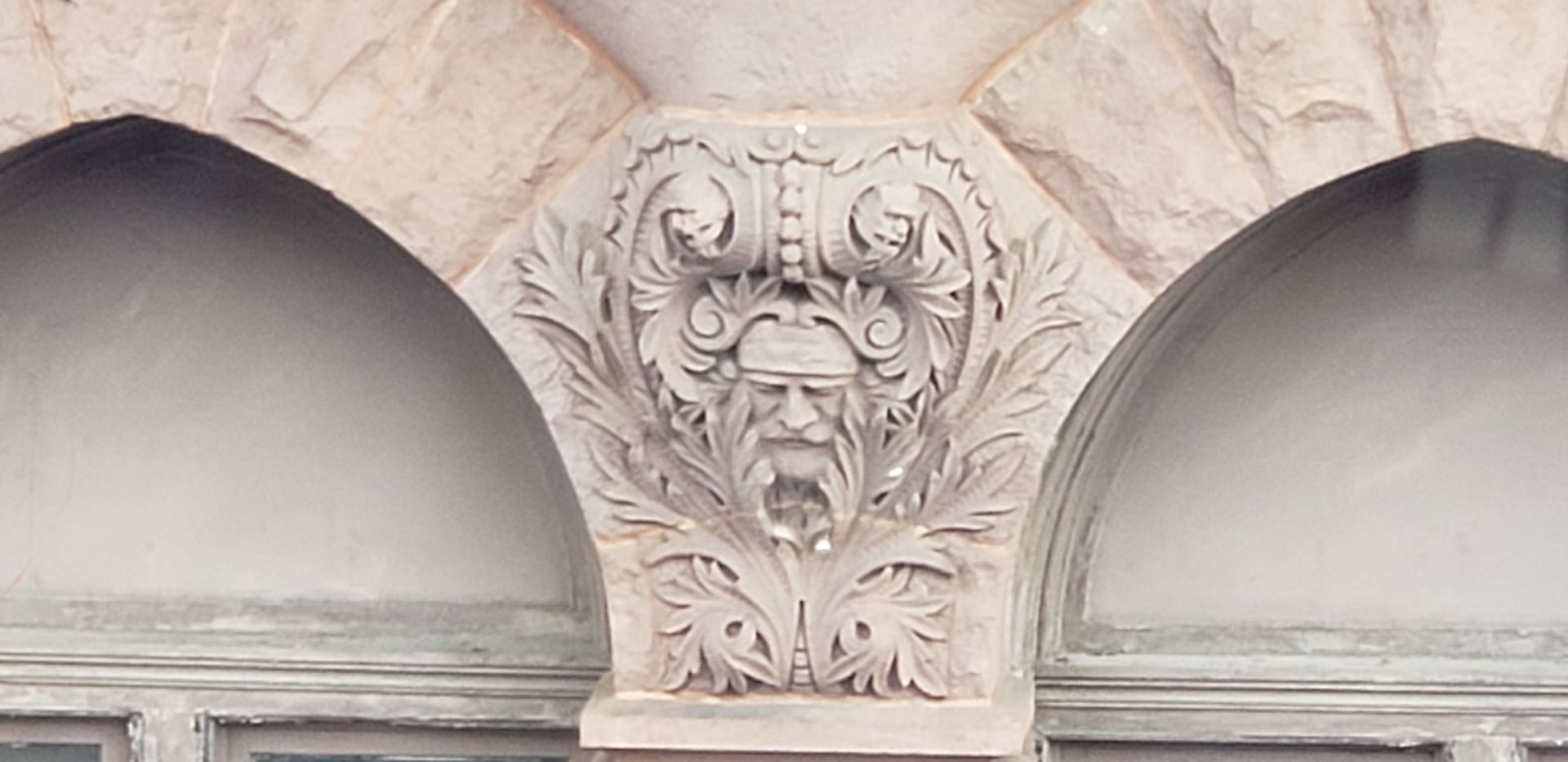 Stone architectural ornament with a carved face between two arched window openings