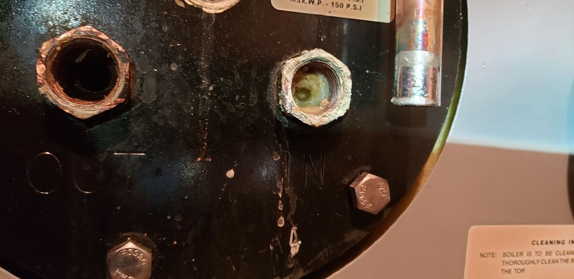 Close-up of a rusty black metal panel with circular holes and a clear tube on the right