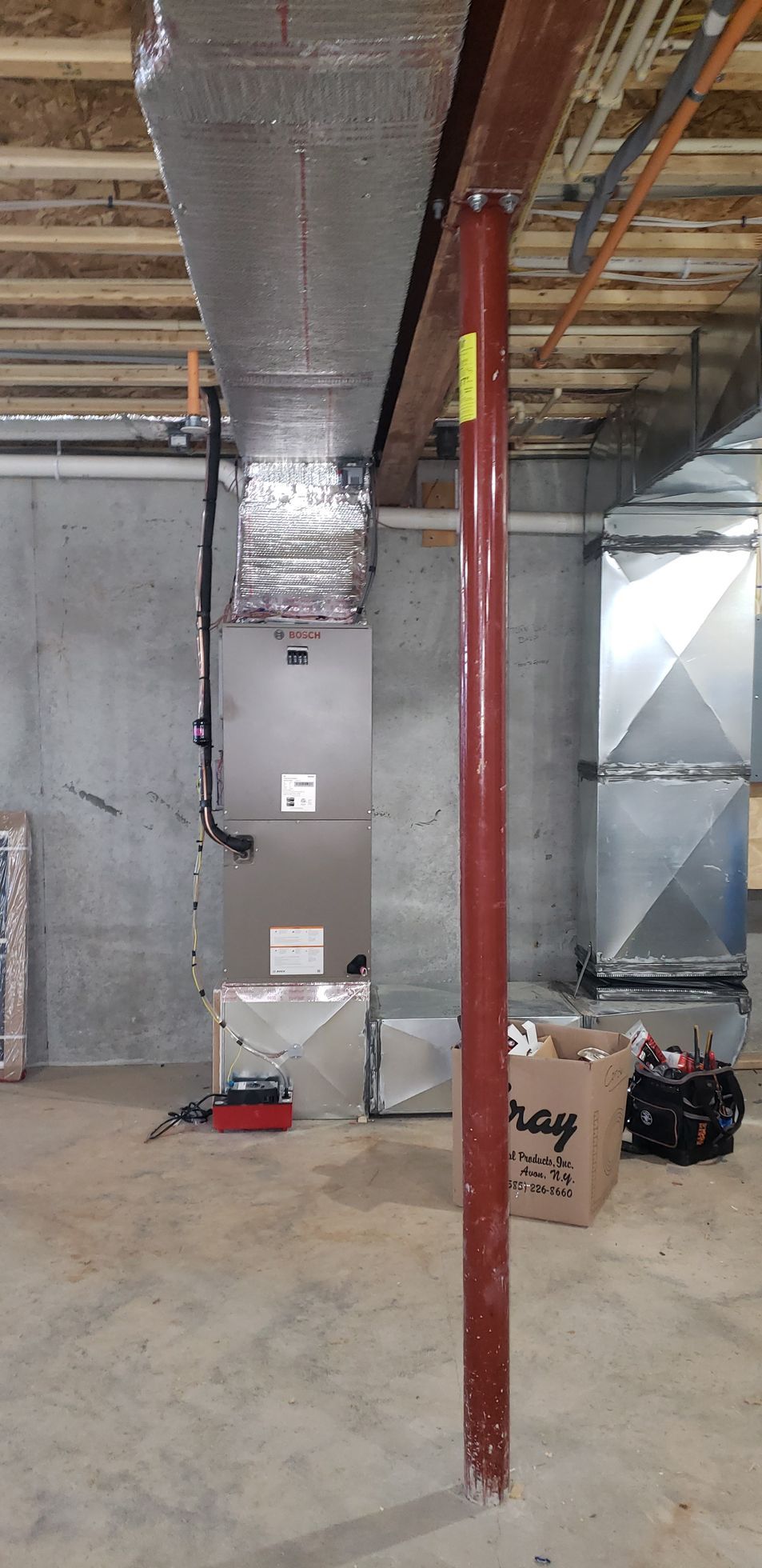 Construction site with exposed ductwork, a red support post, and tools on the floor.