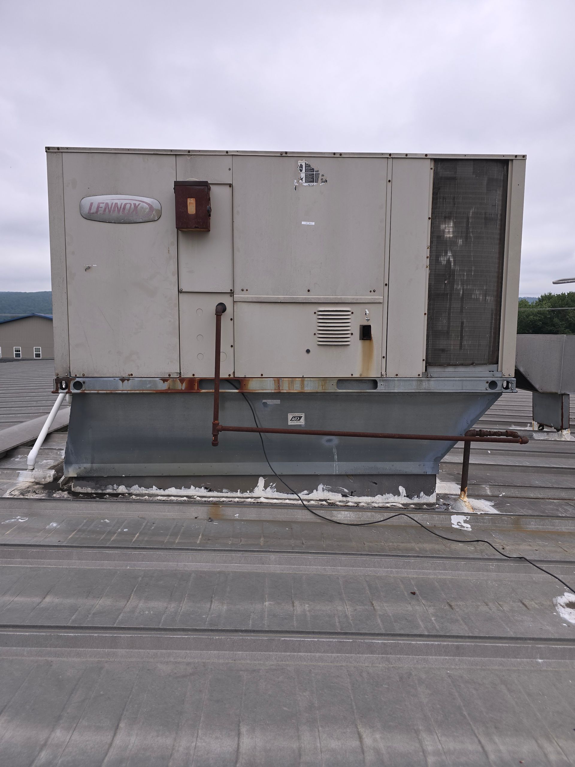 Rooftop industrial HVAC unit on a flat roof with weathered gray walls and snow patches around it